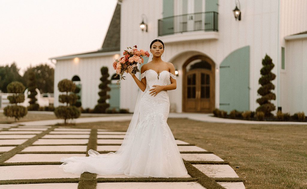 Bride with a floral bouquet standing in front of a french style white wedding venue chapel