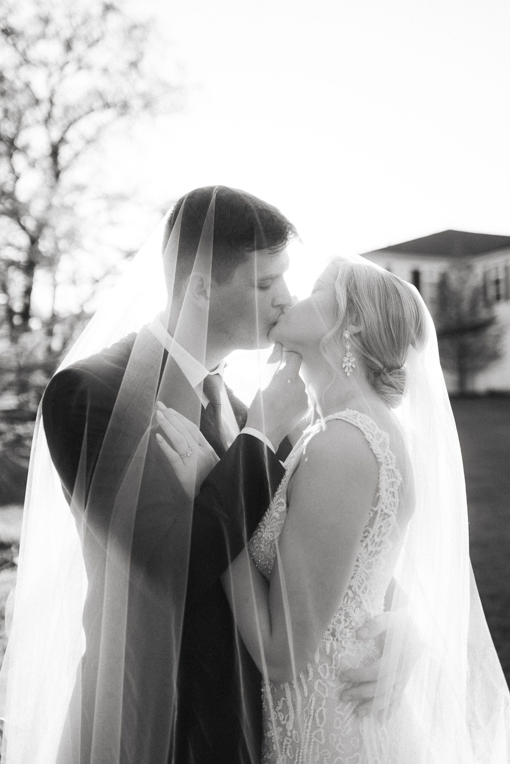 Black and white glowy photo of a newly married couple kissing under the bride's veil at sunset at Rockwall Manor, in Texas