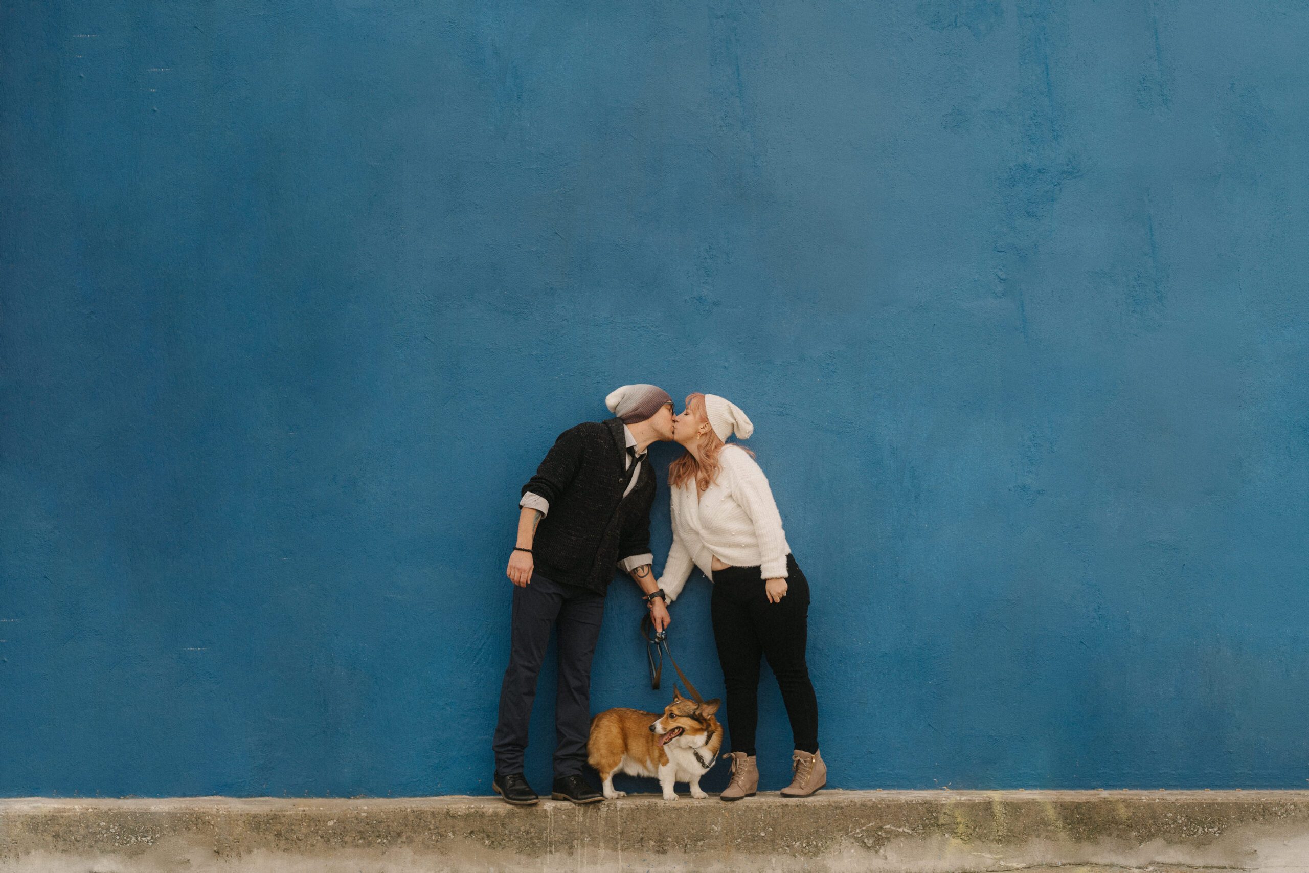 Couple kissing against a blue wall with their Corgi in Denison Texas