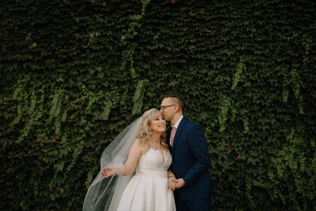 A newly married couple in front of a vine wall at Knotting Hill Place wedding venue in Dallas Texas