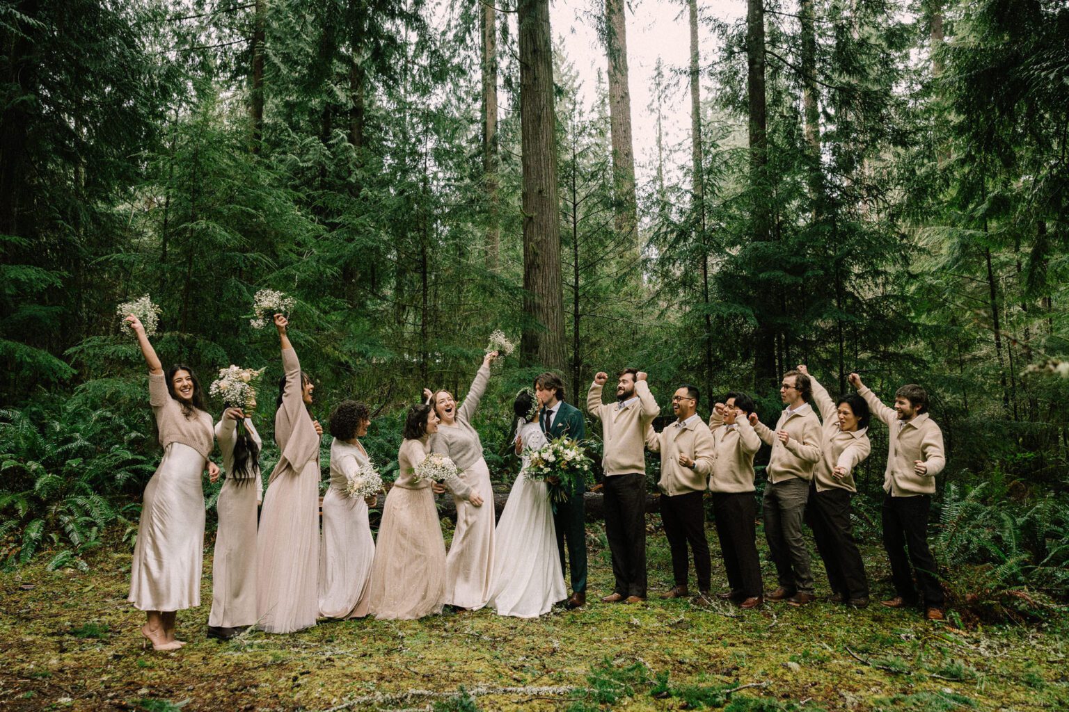 Wedding party celebrating and cheering the bride and groom on their wedding day in a dark green Pacific Northwest forest under the rain