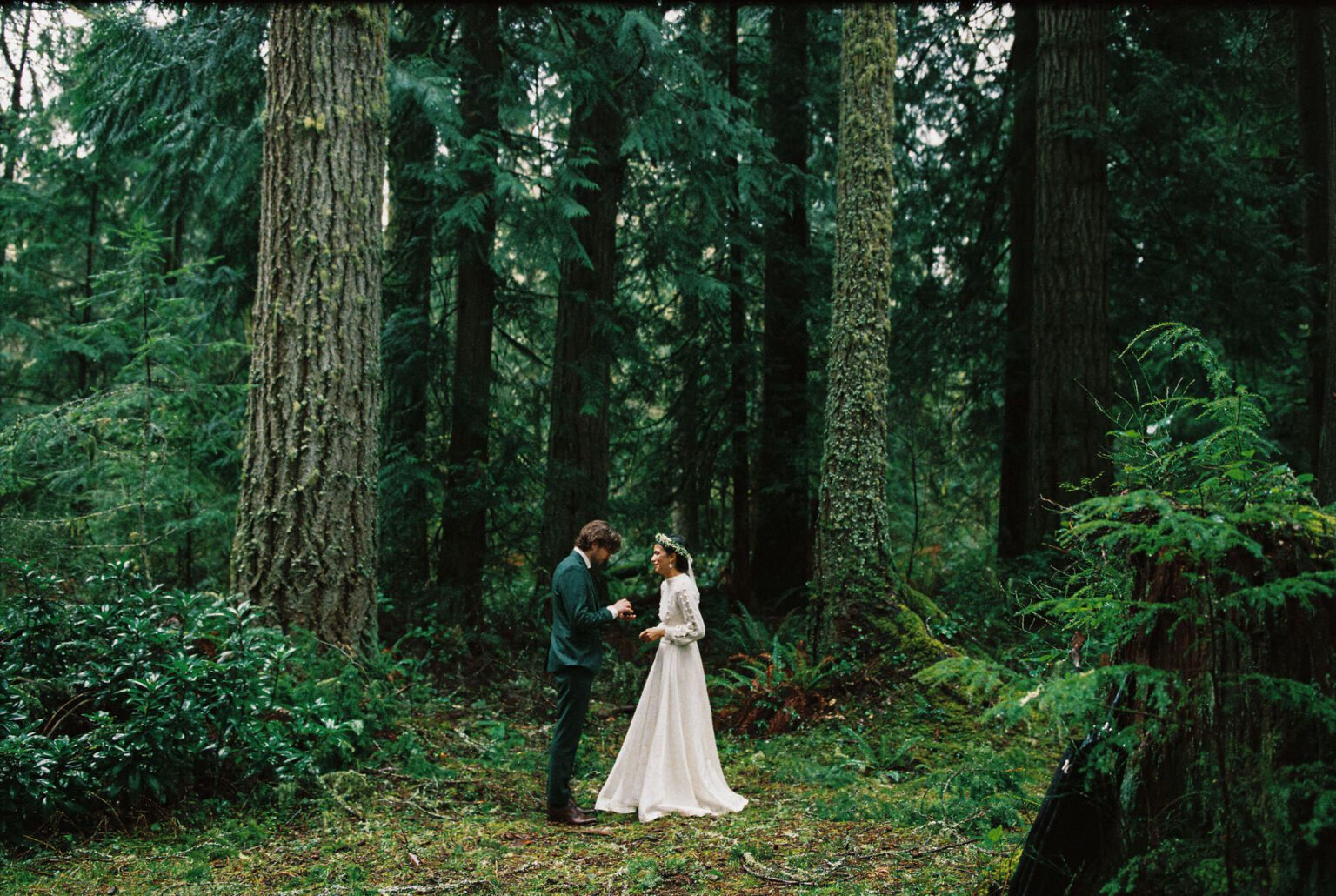 Bride & groom standing together in a dark green Pacific Northwest forest under an umbrella