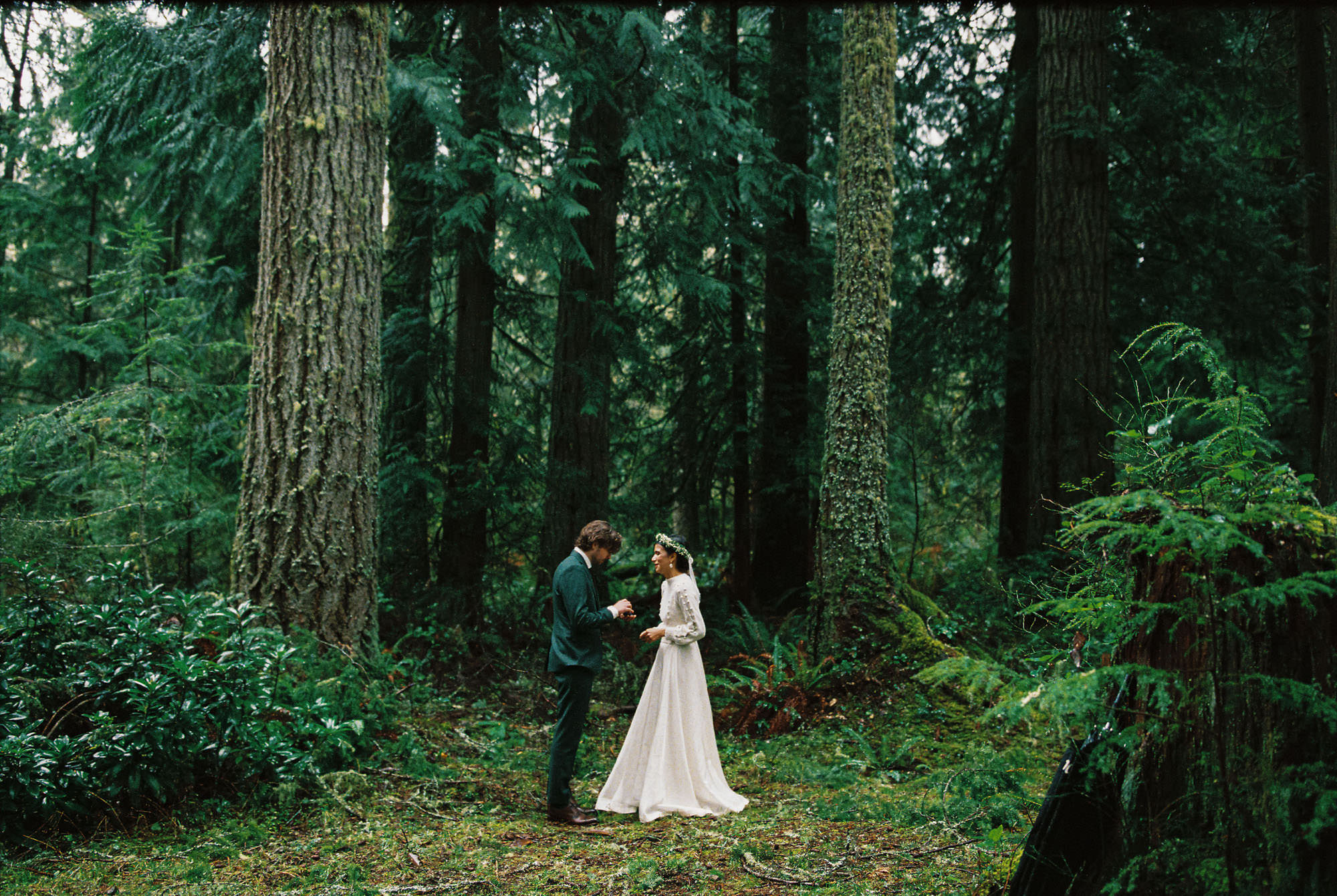 Bride & groom standing together in a dark green Pacific Northwest forest under an umbrella