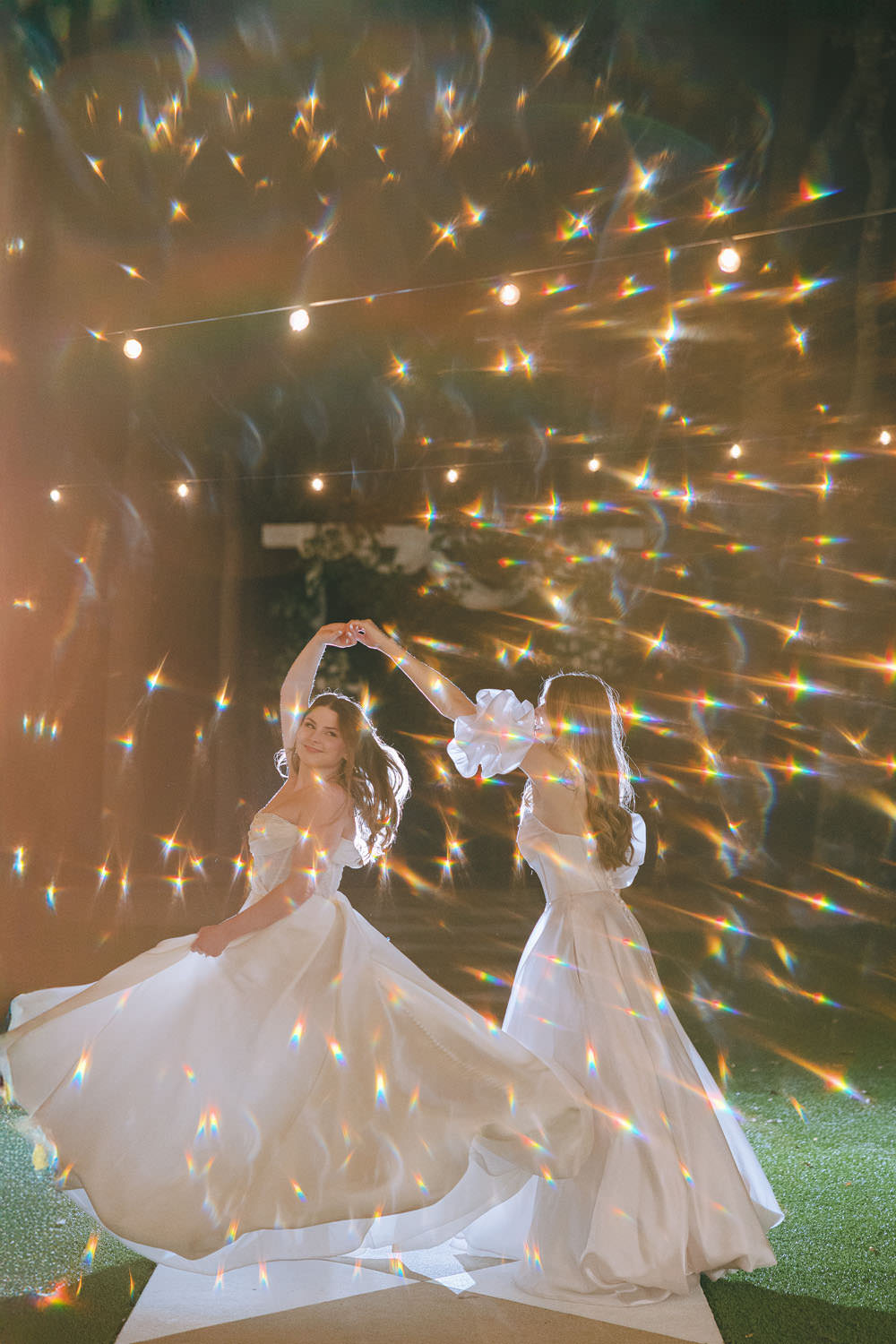 Gay couple wearing wedding gowns on their wedding night, dancing and twirling surrounded by whimsical sparkling lights, at The Rosemary venue in McKinney Texas