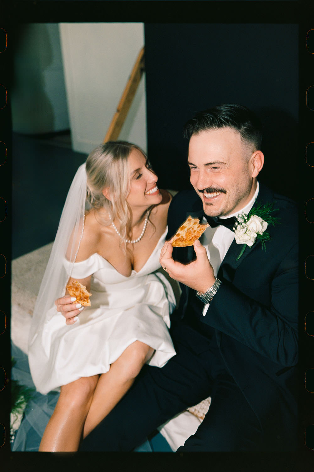 Bride & groom laughing while holding slices of pizza