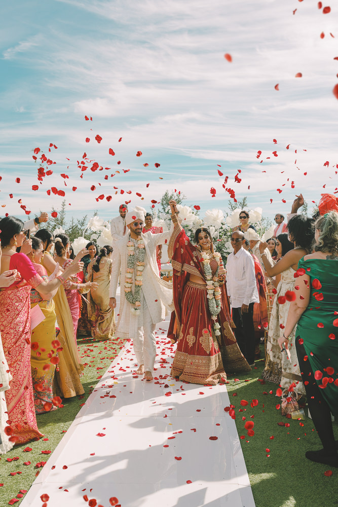 Indian bride and groom walking through a celebratory crowd as they are showered in rose petals on their wedding day in Dallas Texas