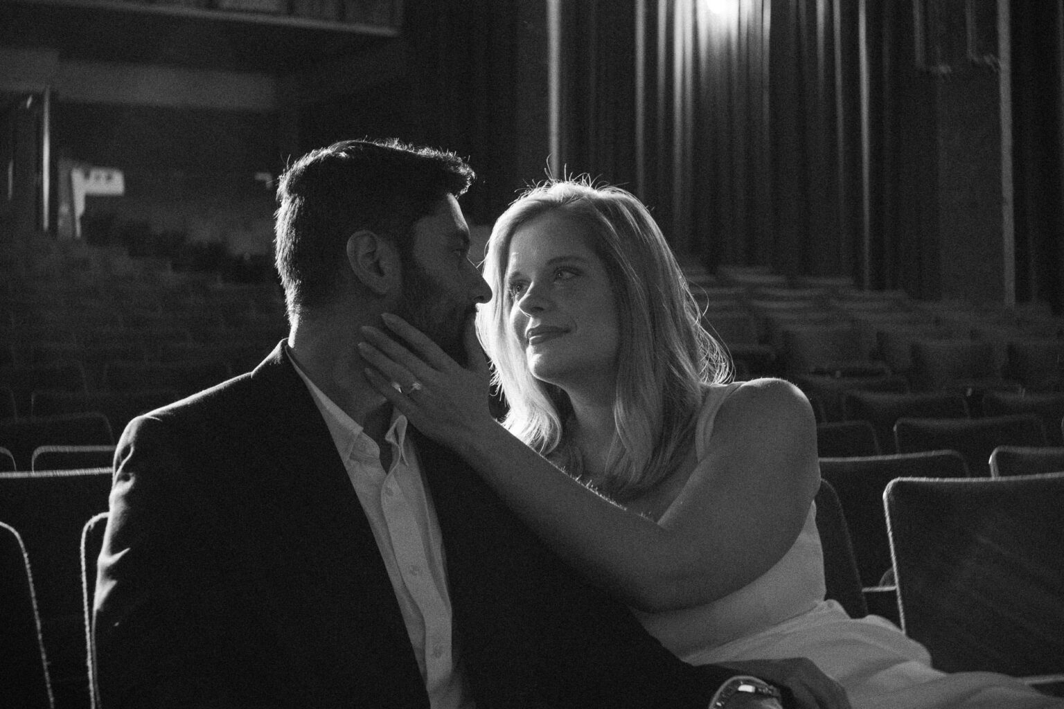 Black and white intimate portrait of two people in a dimly lit movie theater, moody engagement photography Seattle