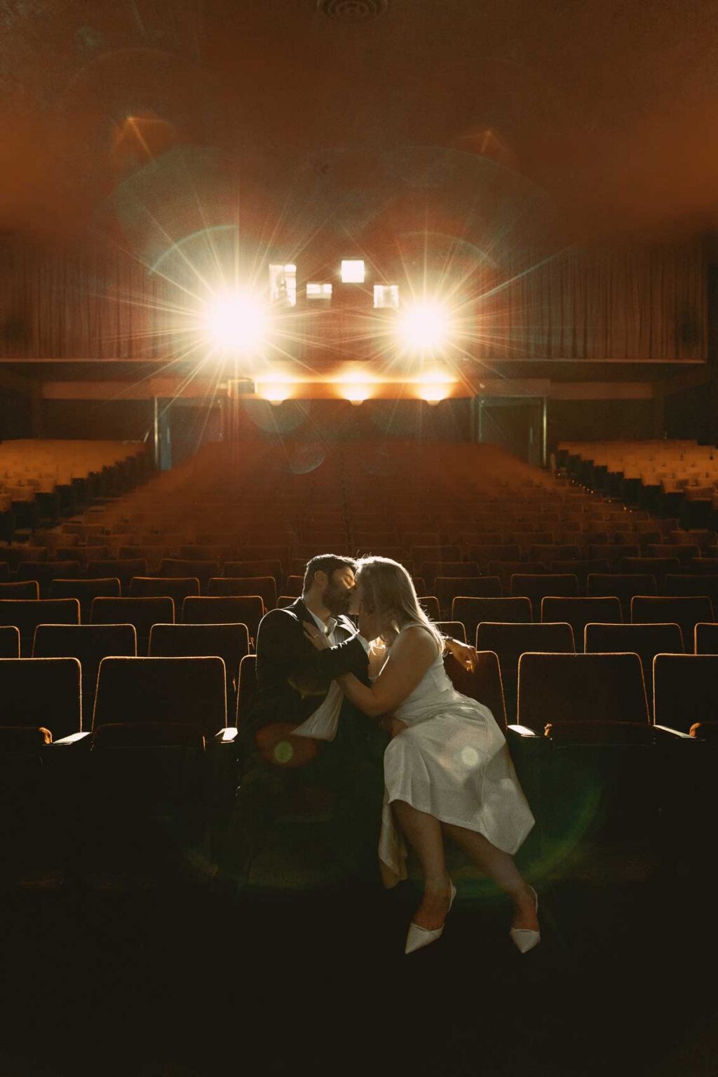 Ginny and Deva embracing in the aisle of SIFF Cinema Uptown Seattle, dramatic theater lighting, film-style engagement photography