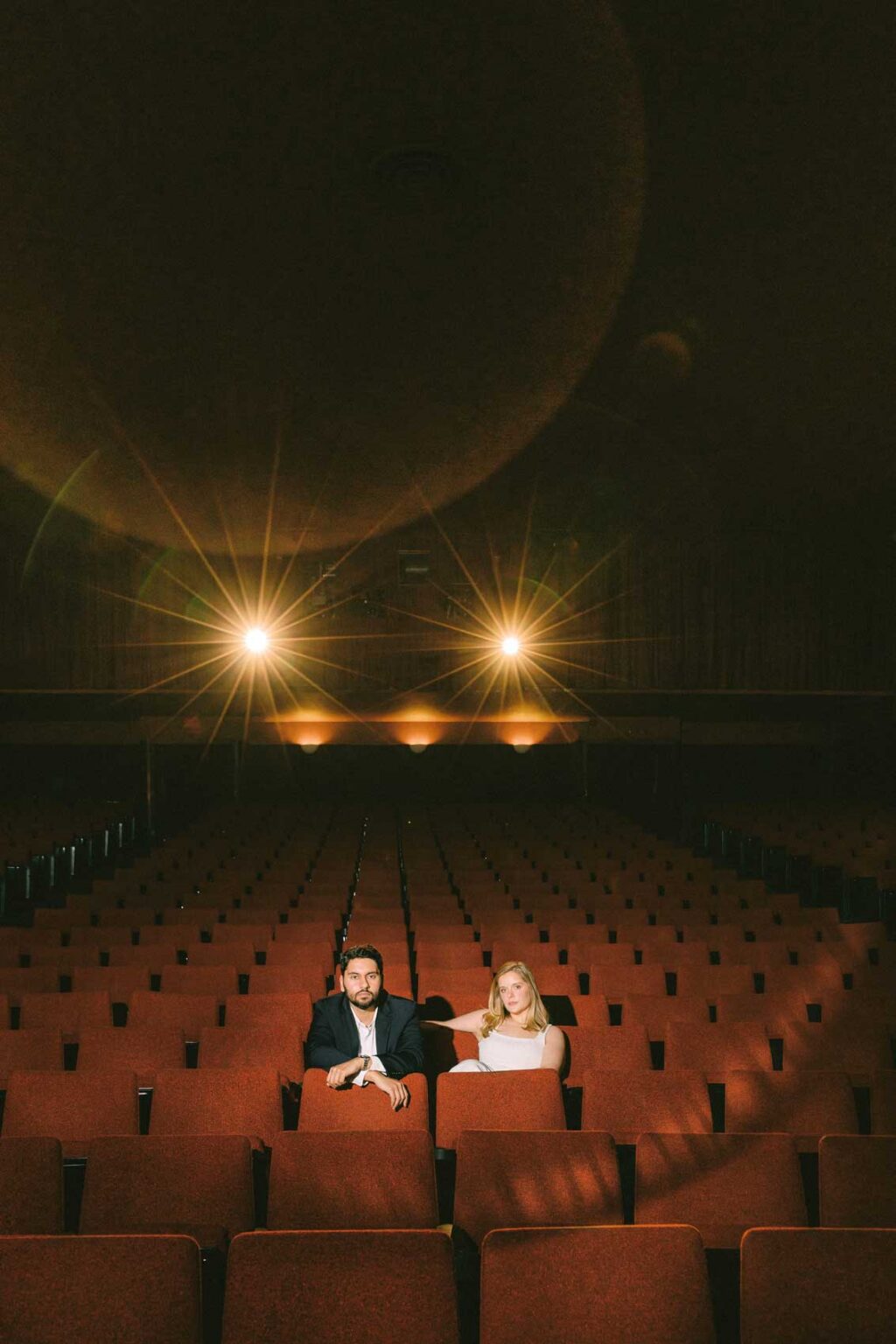 Ginny and Deva embracing in the aisle of SIFF Cinema Uptown Seattle, dramatic theater lighting, film-style engagement photography