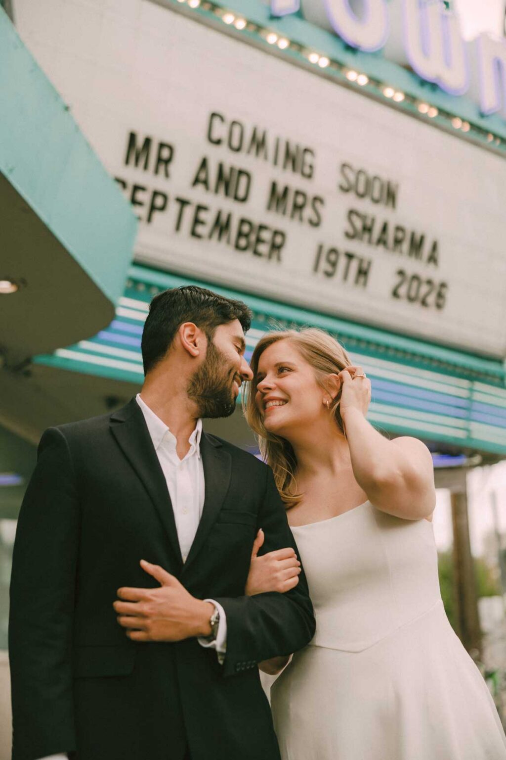 Couple standing beneath a lit movie theater marquee sign with their wedding date, SIFF Cinema Uptown Seattle